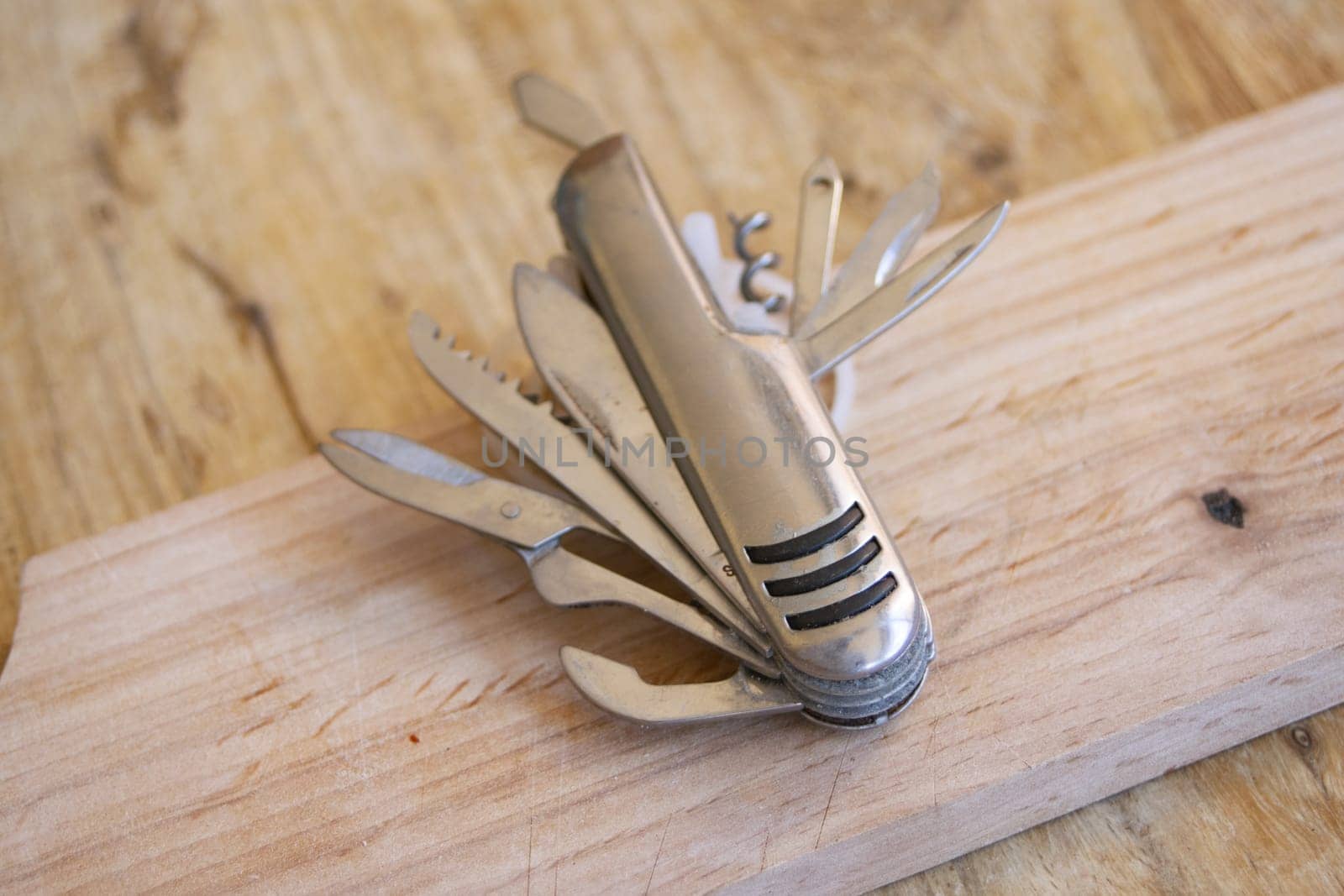 A versatile silver multi-tool knife with several blades and tools extended, lying on a textured wooden surface