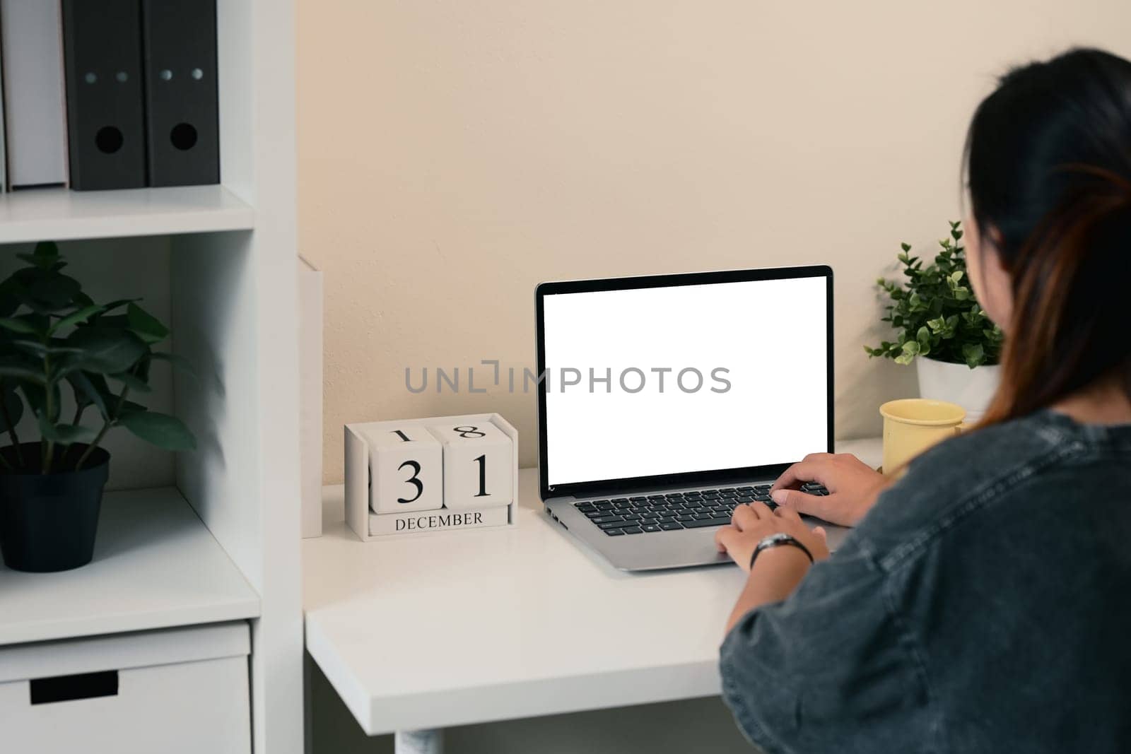 Rear view of young woman working on a laptop at a minimalist desk.