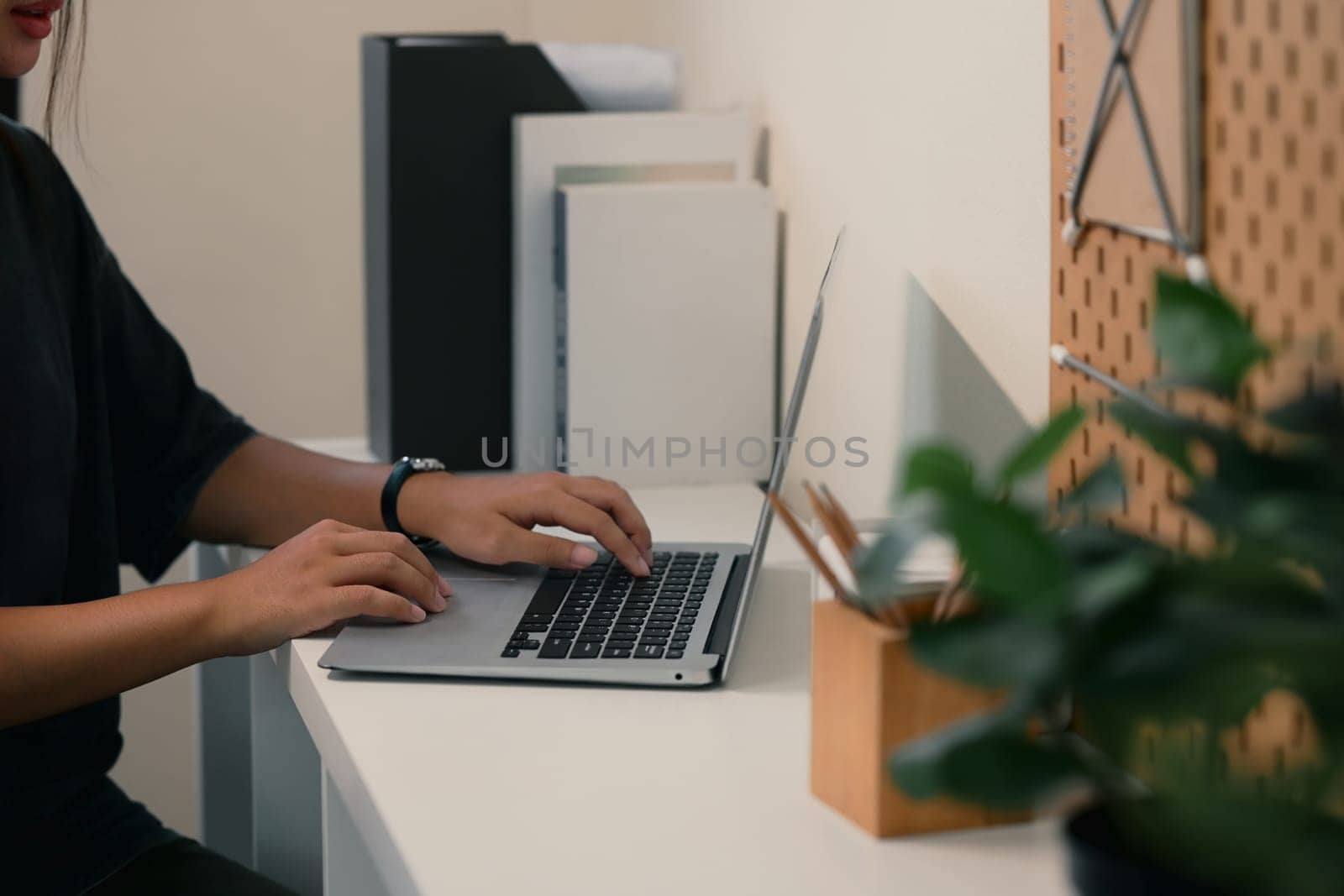 Side view of young woman working on a laptop in a tidy home office.