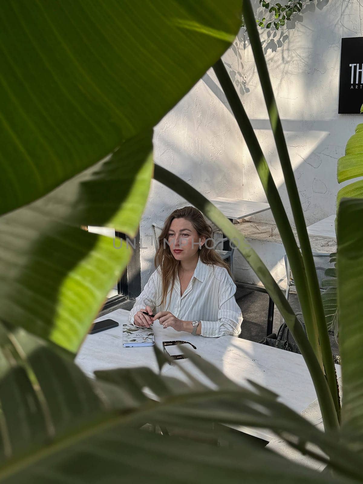 A woman sits at a table in a bright, modern workspace, focused on her tasks amid vibrant green plants.