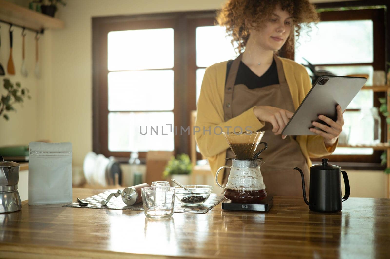 Young woman uses digital tablet while preparing pour over coffee in a stylish kitchen.