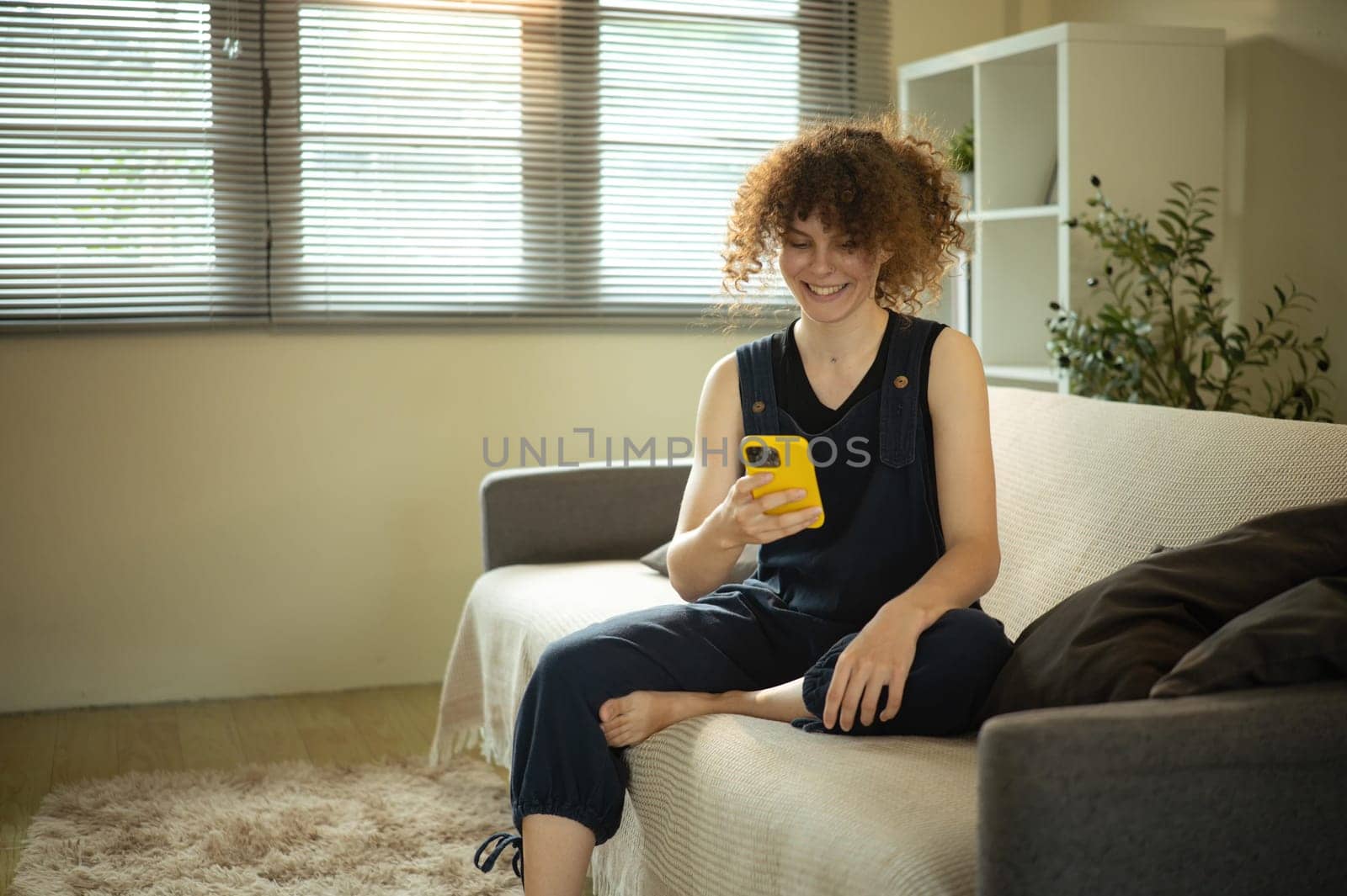 Relaxed young woman smiles while using her smartphone on a cozy couch.