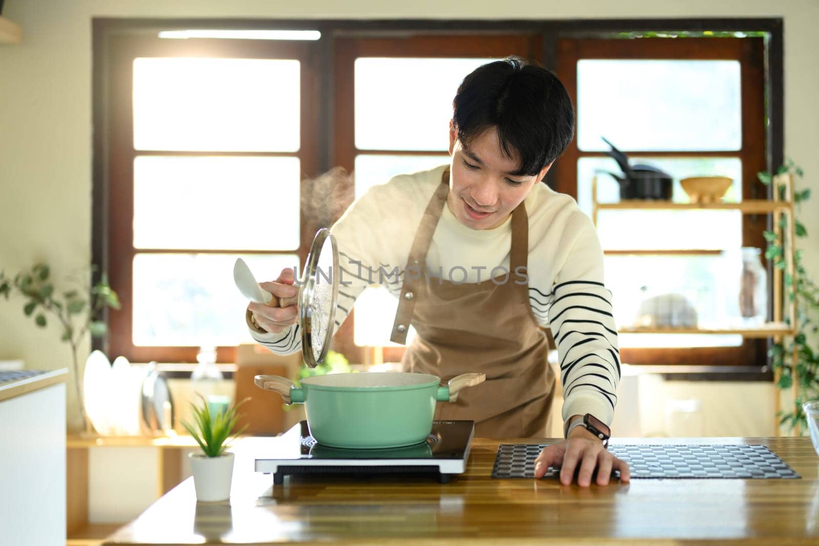 Smiling man in an apron preparing meal in a sunlit modern kitchen.