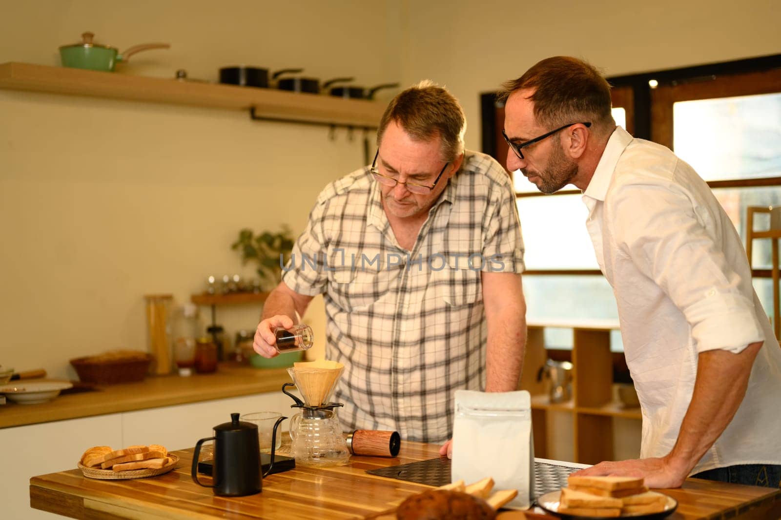 Mature father and adult son preparing fresh pour-over coffee in a cozy kitchen.