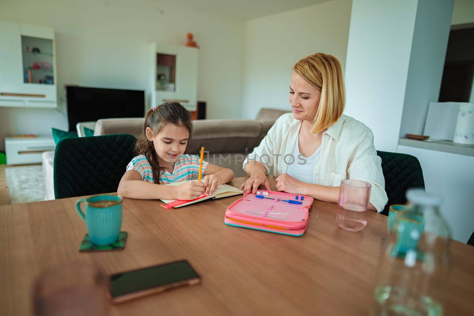A mother guides her daughter while she writes in a notebook.
