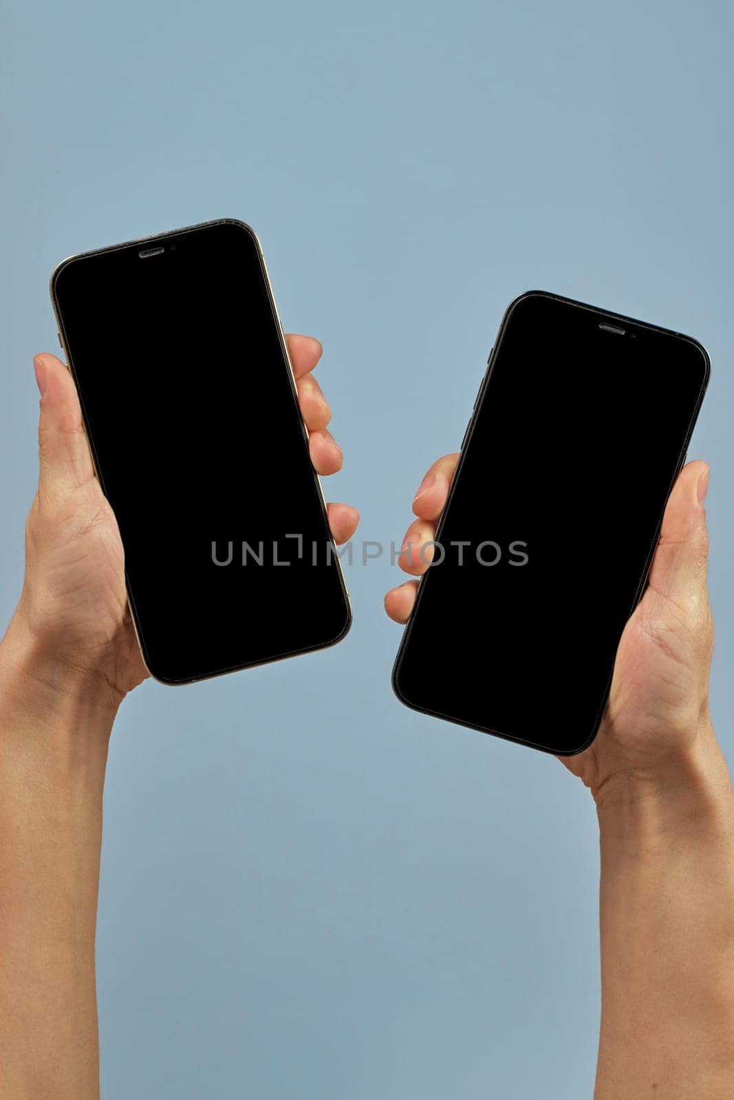 woman holding two smartphones with blank screens on blue background
