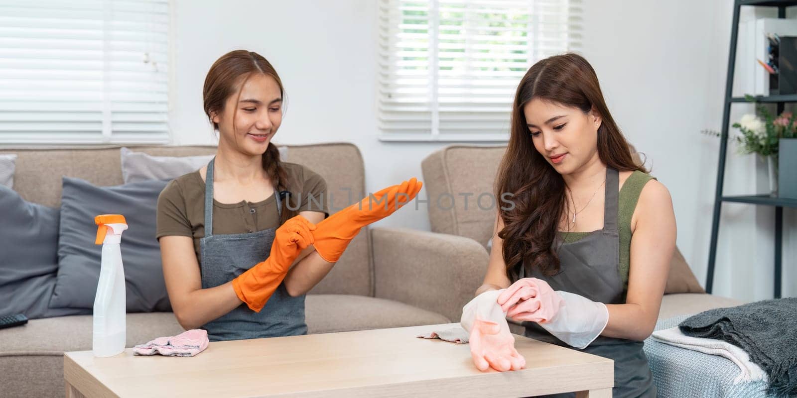 Two women prepare for cleaning by putting on gloves, showcasing the importance of protection and readiness in household chores.