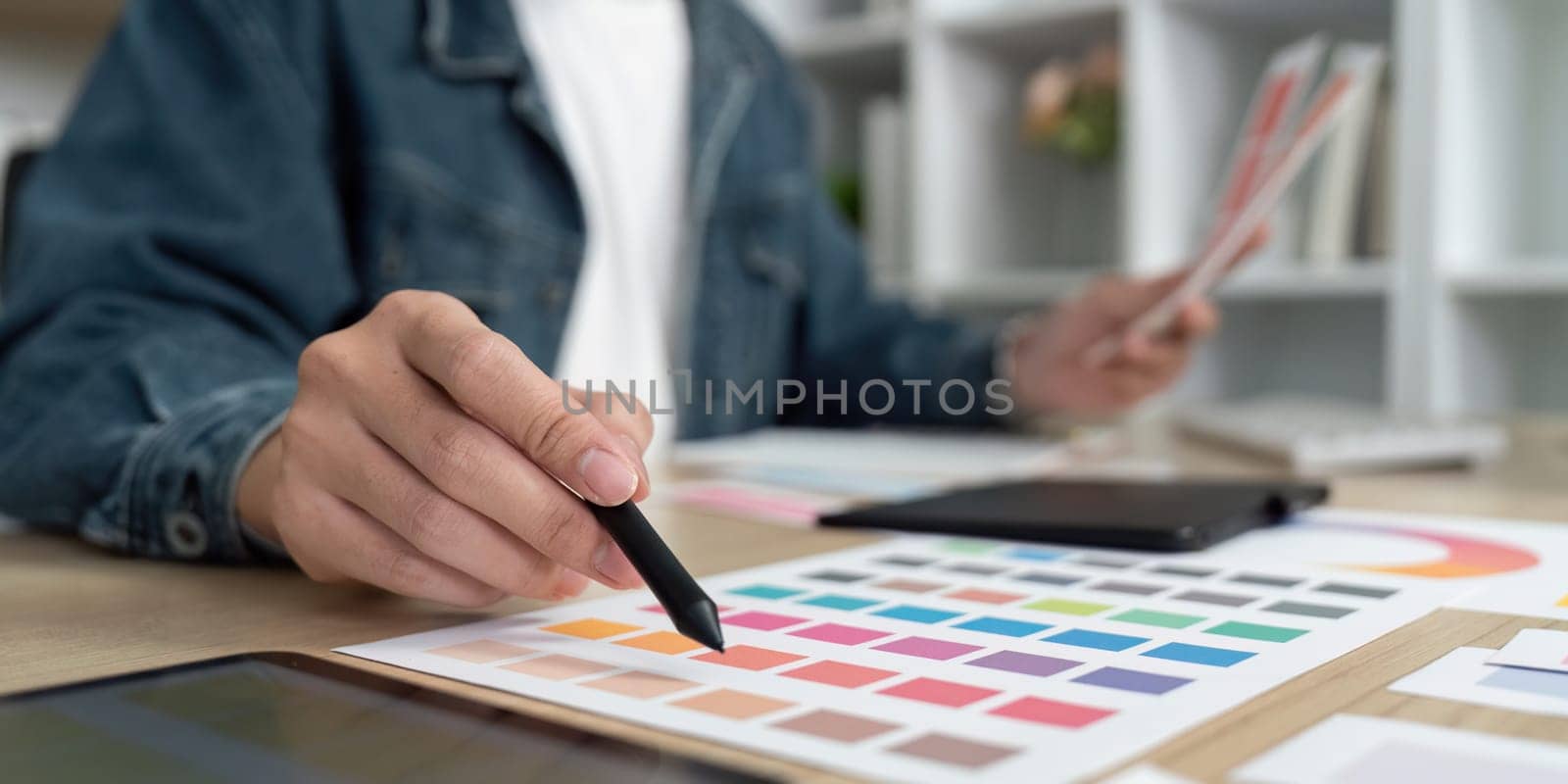 A designer carefully analyzes color schemes and layouts using swatches and a digital tablet in a stylish workspace.