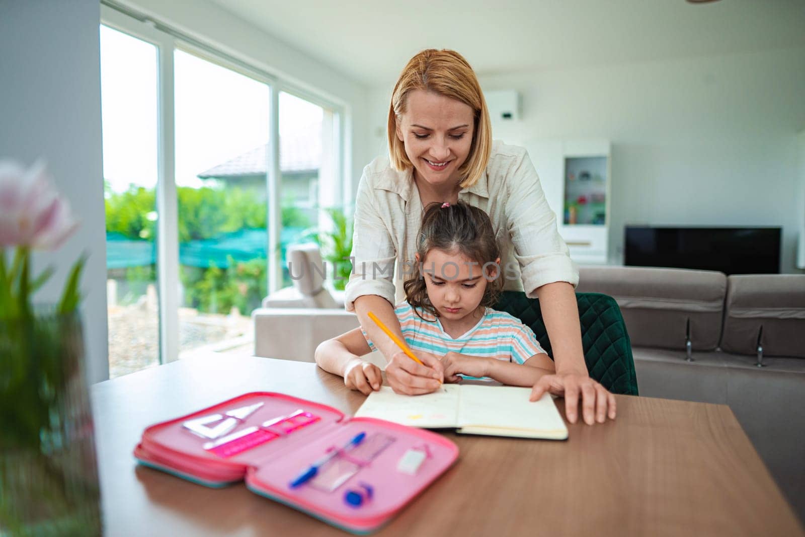 A mother guides her daughter as they study together happily.