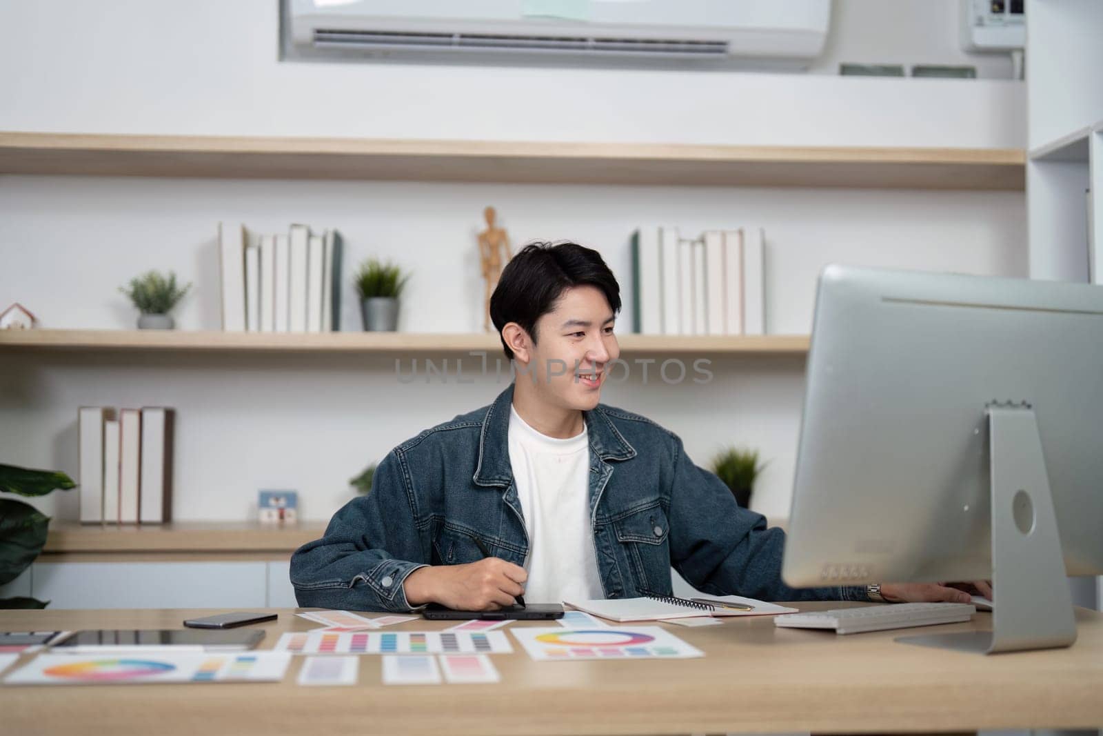 A young designer focused on his computer screen in a modern workspace, showcasing a productive design environment.