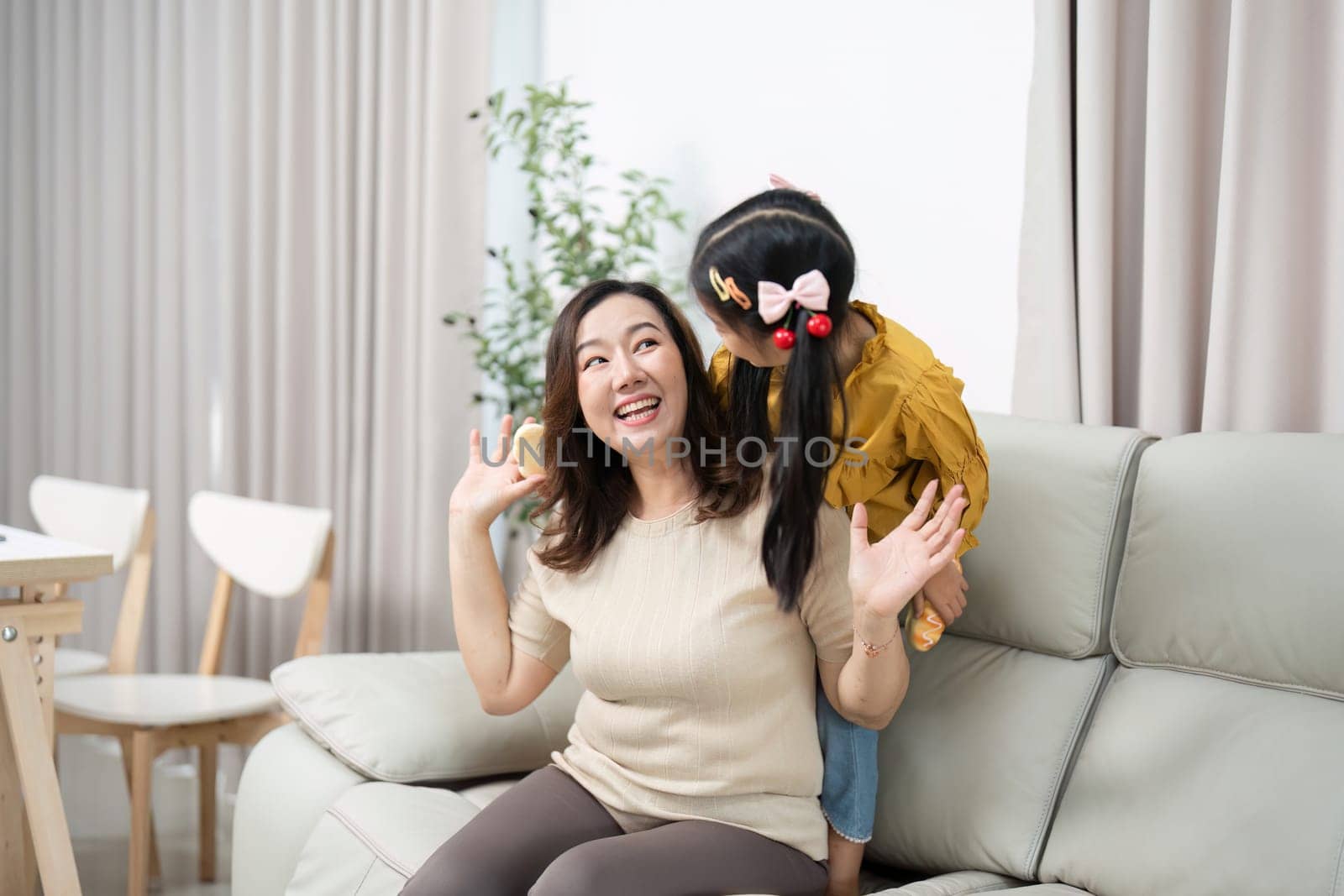 A mother enjoys playful moments with her daughter, showcasing their close bond and happiness in a cozy living room setting.