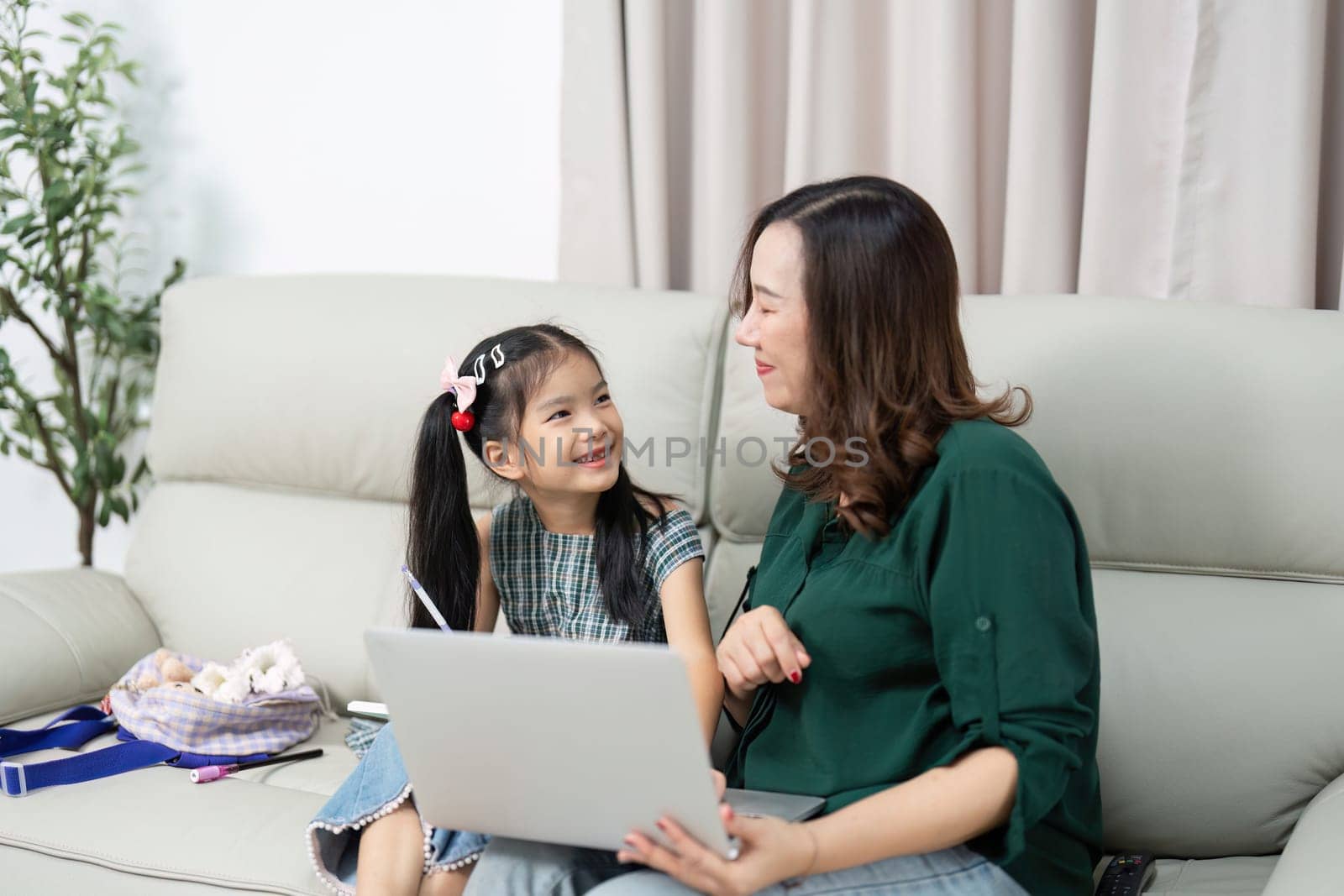 A mother and her daughter sit together on a couch, engaging in a learning activity on a laptop. This image captures the essence of back-to-school preparations and family support.