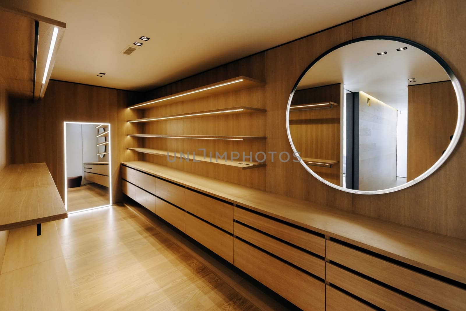Theres a spacious walkin closet featuring elegant wooden shelves expertly crafted, accompanied by a beautiful round mirror enhancing the overall aesthetics