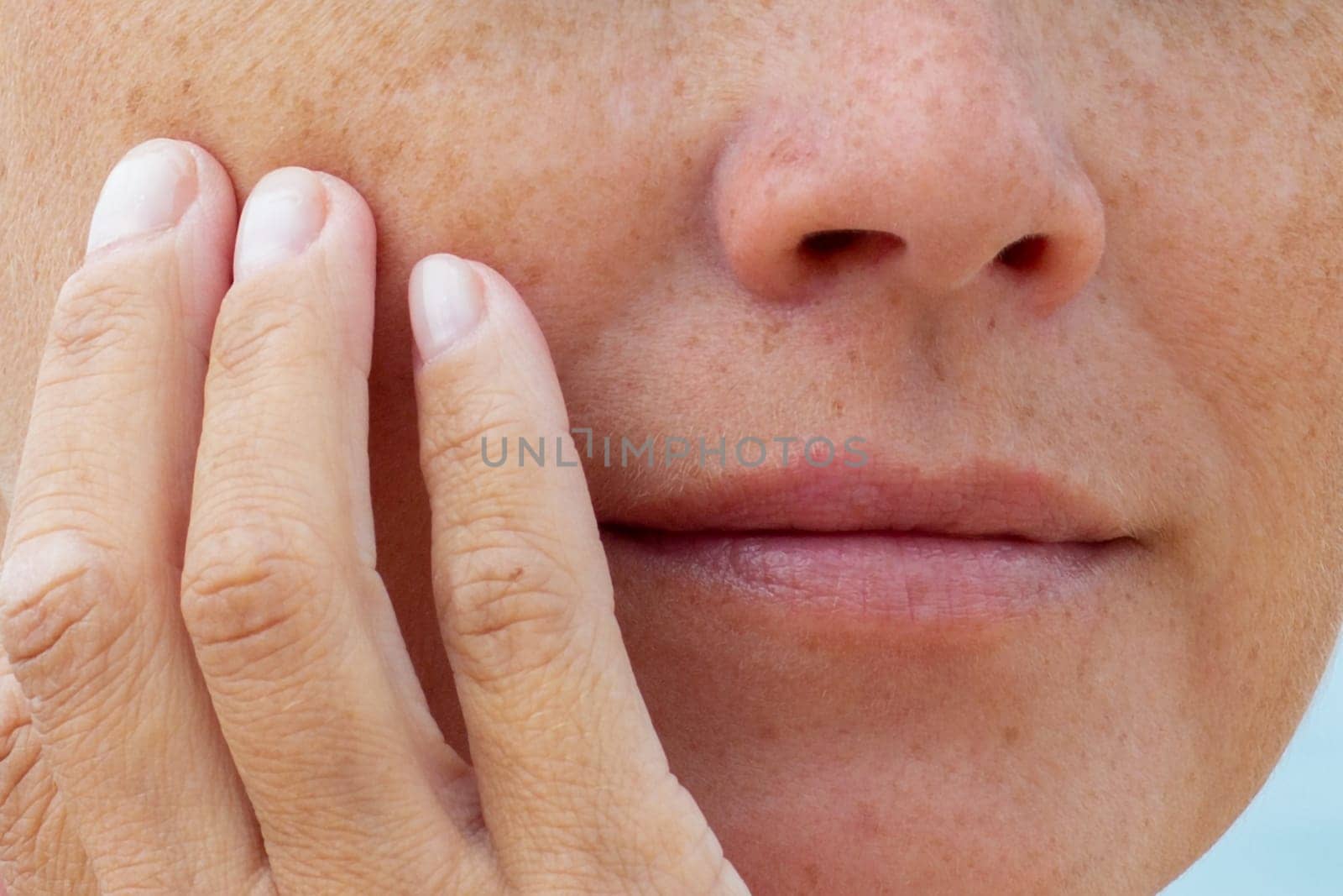 Close-up of woman touching her cheek with fingers showing natural skin texture and freckles