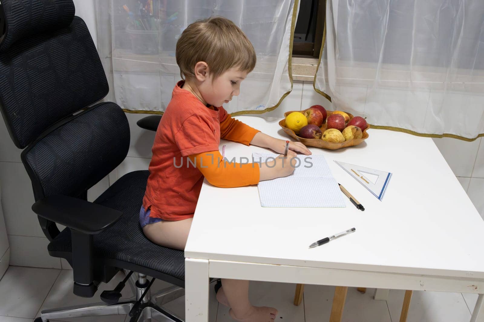 Young boy writing on notebook sitting on an ergonomic office chair in his home