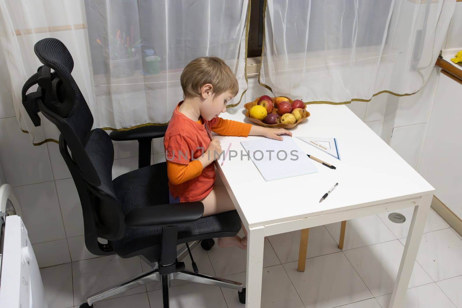 Young boy drawing on a notebook while sitting on an ergonomic chair at the kitchen table