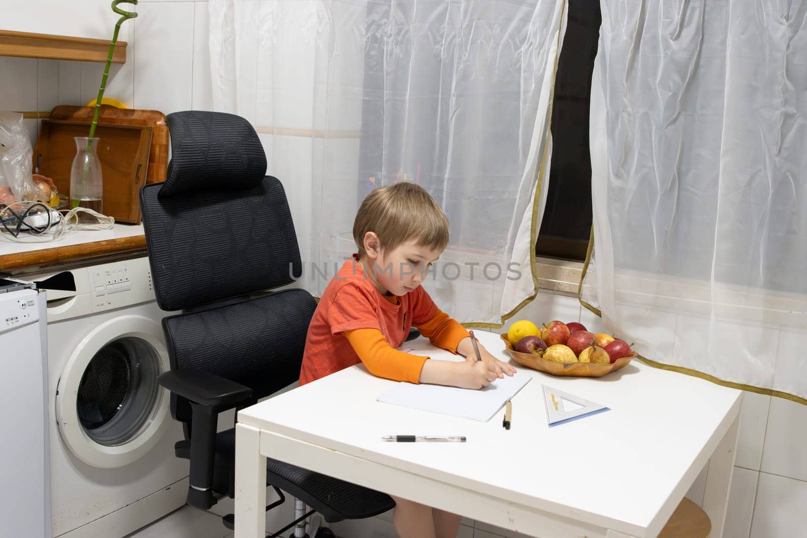 Preschooler concentrating on drawing at a white table with fresh fruits, showcasing a domestic learning environment