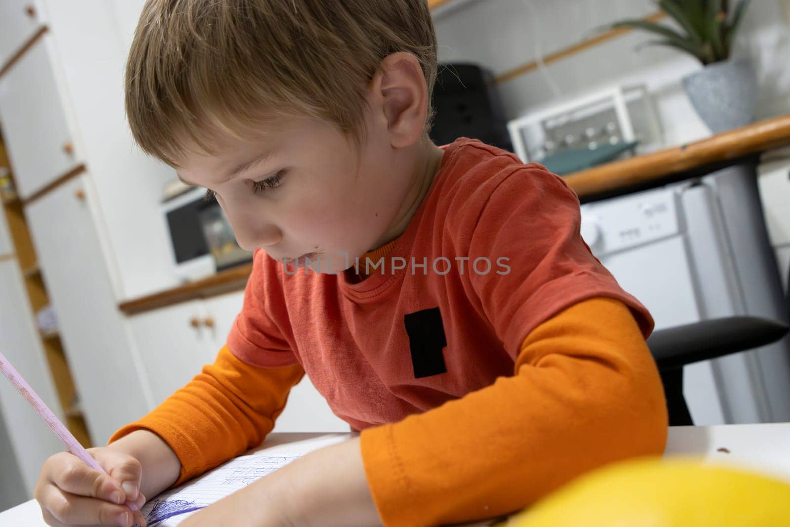 Preschooler concentrating on drawing with a colored pencil at the kitchen table