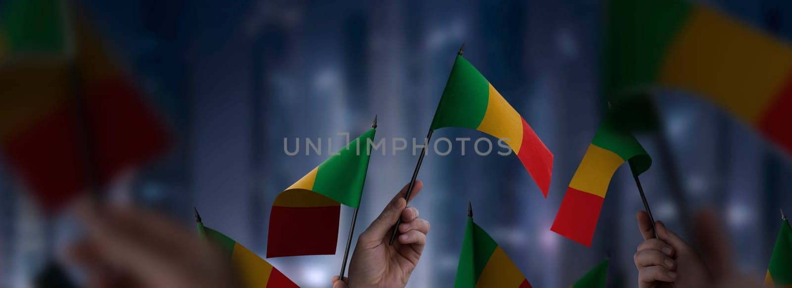 Mali flags in their hands on a blurred urban background. The photo illustration was created without the use of artificial intelligence, only using Photoshop.