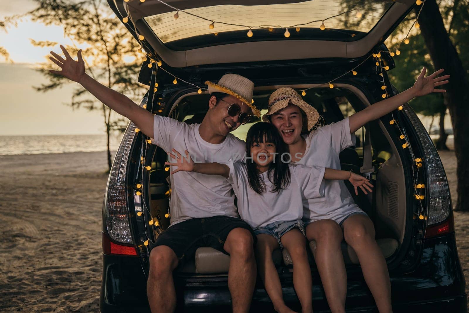 Asian family sitting back car to beach at sunset feeling funny in holidays and relaxation together. Dad, mom and daughter happy weekend travel enjoy at beach. summer vacation travel camping road trip