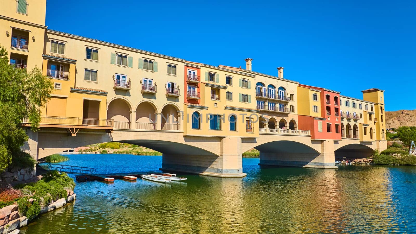 Aerial view of a Mediterranean-style bridge and luxury waterfront buildings at Lake Las Vegas Nevada with colorful facades boats and tranquil water under a bright blue sky perfect for travel and real estate themes