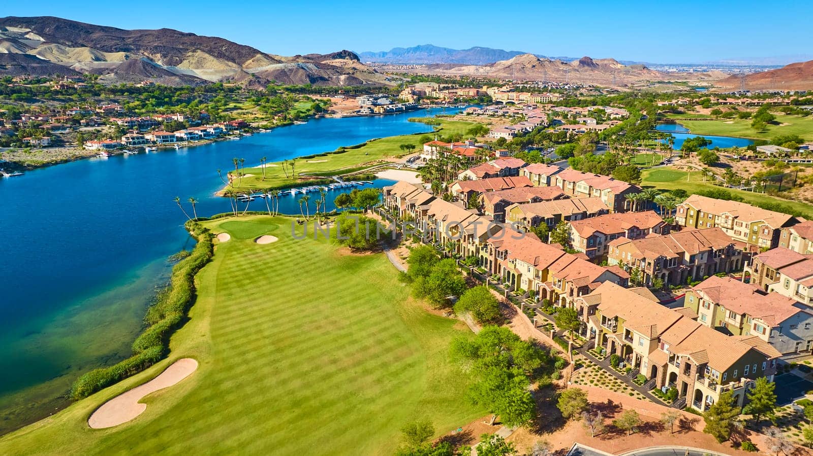 Aerial view of a luxury lakeside community in Lake Las Vegas Nevada featuring a lush golf course sparkling blue water and upscale townhomes surrounded by desert mountains on a bright sunny day