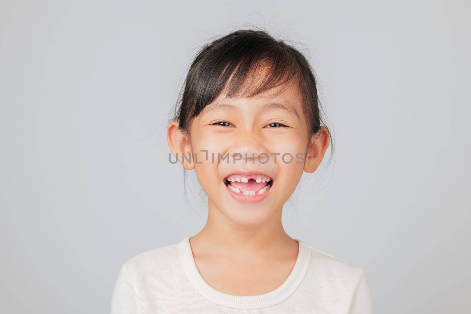 Tooth loss lesson by dentist for happy Asian girl, smiling with missing tooth. Kid shows gap, learning dental care and growing healthy new teeth after loss. isolated white background