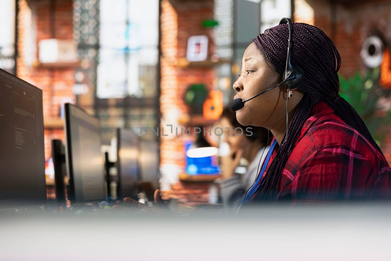 Call center representative in office helping customers by answering questions, close up shot. African american woman in customer support workspace using headset to talk with clients