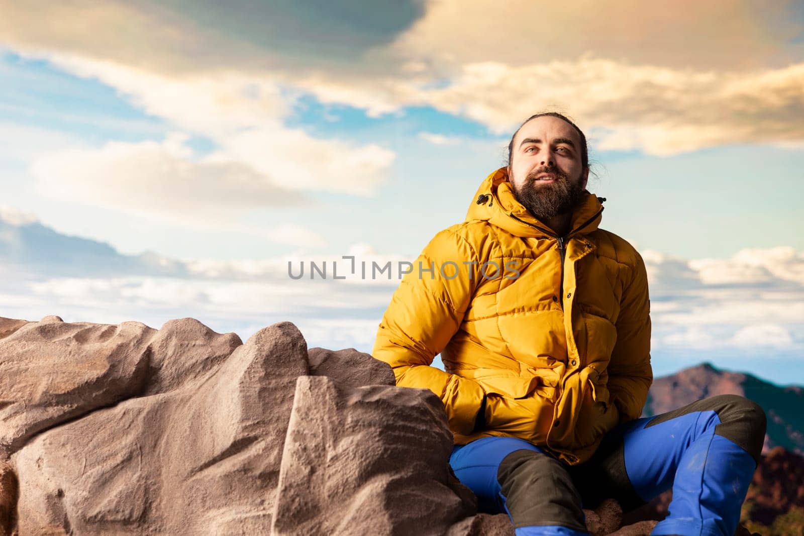 Male hiker looks out over a breathtaking mountain range from the hill top, embracing the solitude and fresh air of the great outdoors. Sense of adventure and endless nature exploration.