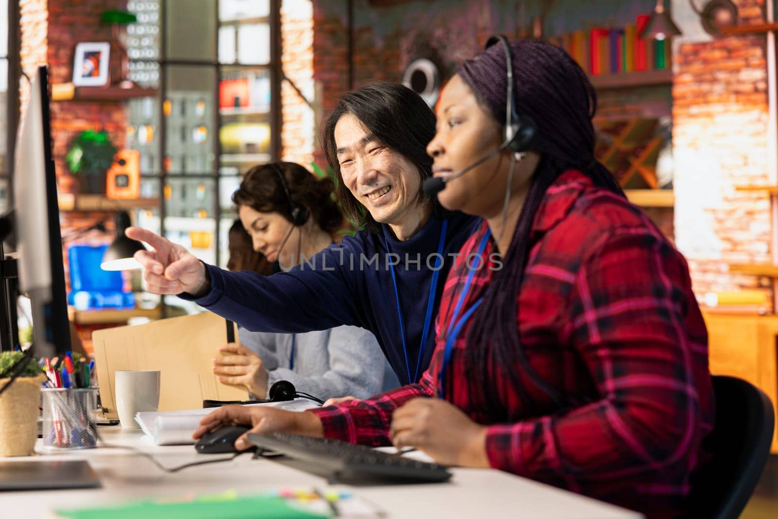 Happy customer service senior manager teaching new employee how to track support tickets in company software. Cheerful Asian call center supervisor shows intern how to create and close support tickets