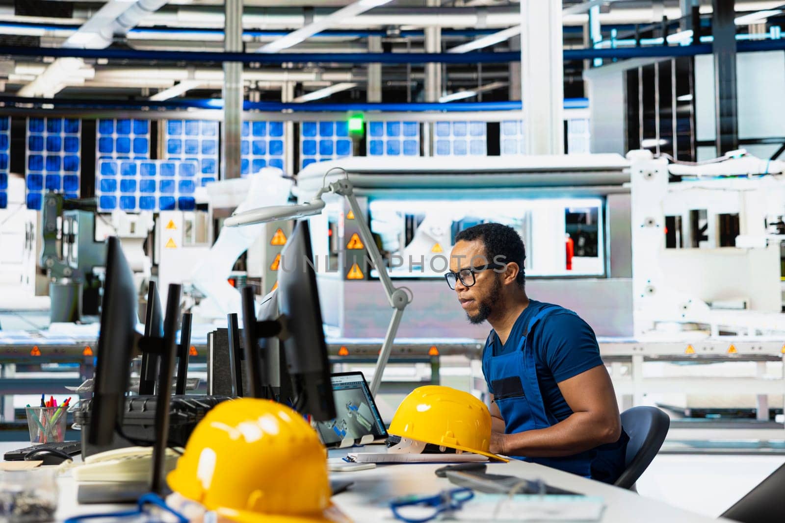 Male engineer using pc setup to oversee solar panel plant assembly lines, troubleshooting photovoltaic system to manage seamless production line with robotic arms. Renewable energy.