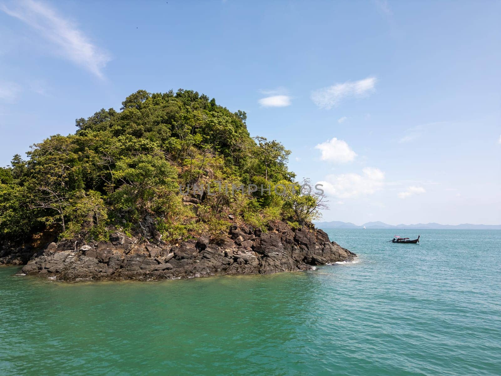 Drone shot of a sailboat cruising along Thailand exotic coastline, breathtaking scene of a motorboat navigating the turquoise waters. Passing by scenic coastal cliffs and a tropical shoreline.