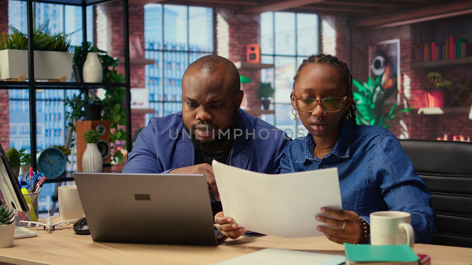 Two remote employees examining calendar appointments on their documents, checking papers and laptop information to solve important tasks on schedule. Couple collaborating at home. Camera A.