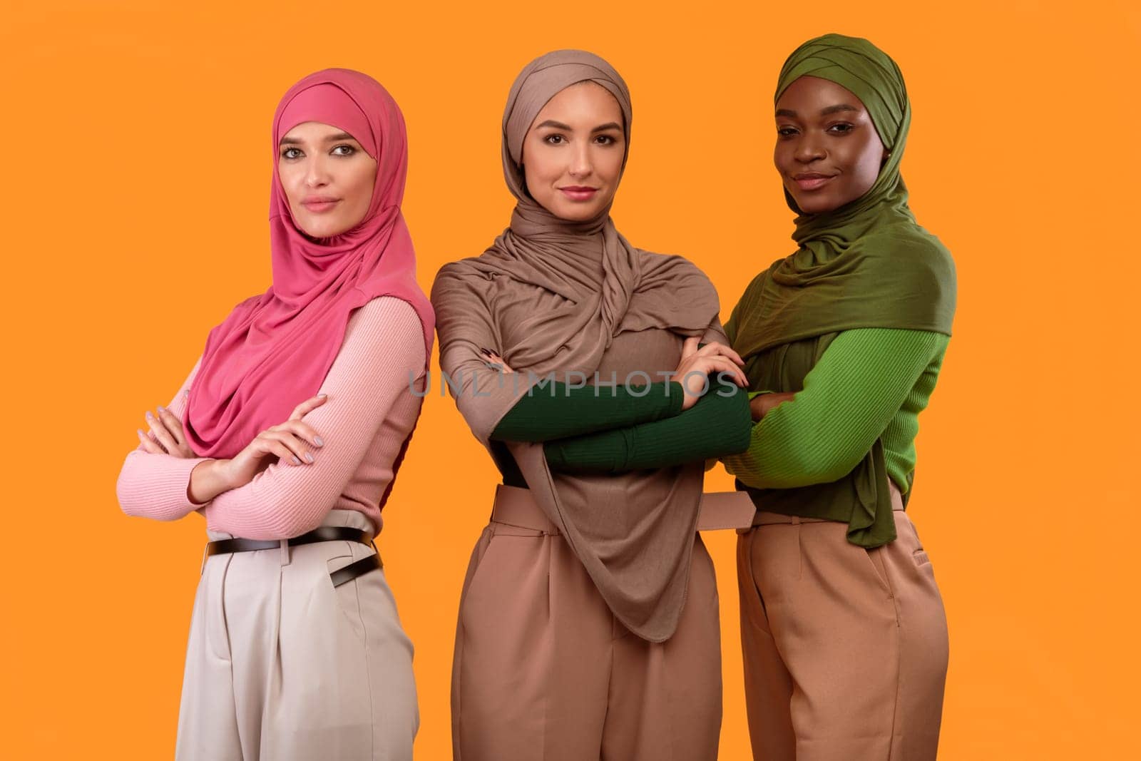 Three Gorgeous Diverse Muslim Ladies In Hijab Posing Crossing Hands Smiling To Camera Standing Together On Yellow Studio Background. Arabic Female Beauty And Fashion Concept