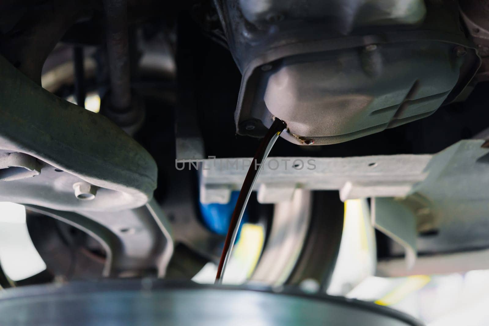 Car mechanic drain the old lubricant engine oil at car garage for changing the oil in a car engine