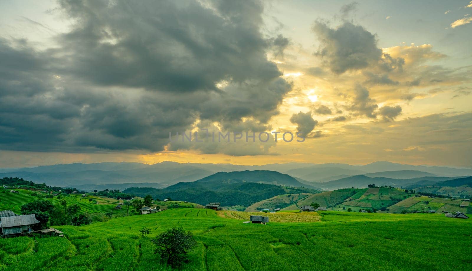 Sunset casts golden light over rolling green hills and rice terrace fields with rural village in the mountains. Eco living and sustainable agriculture. Organic farming. Beauty of sustainable living.