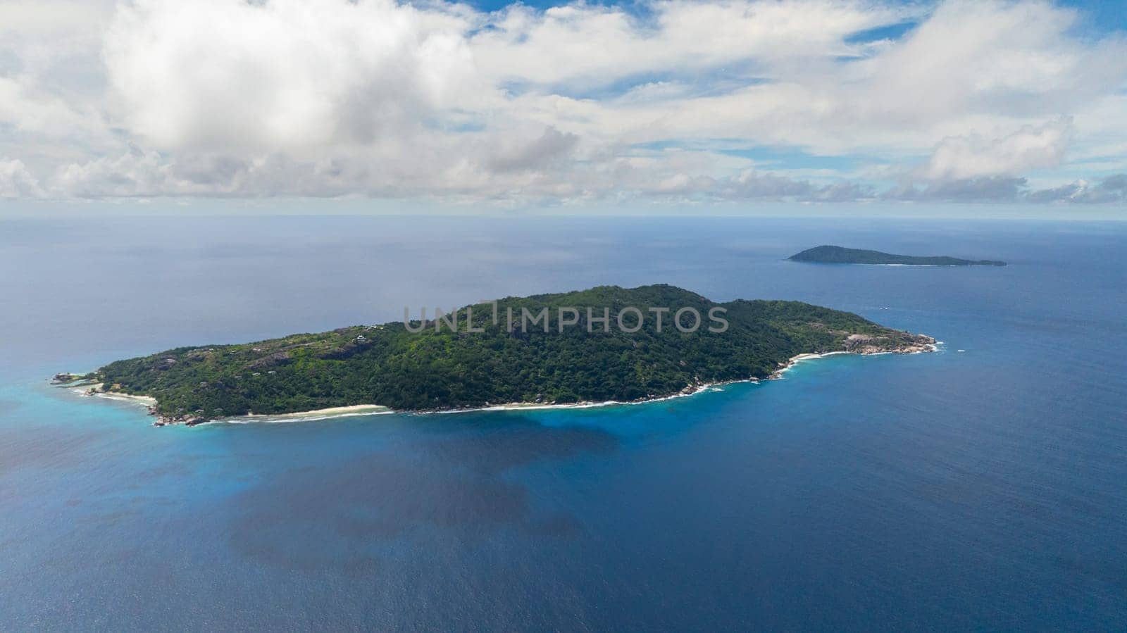 A distant island surrounded by deep blue ocean and greenery under a cloudy sky. Felicite, Seychelles.