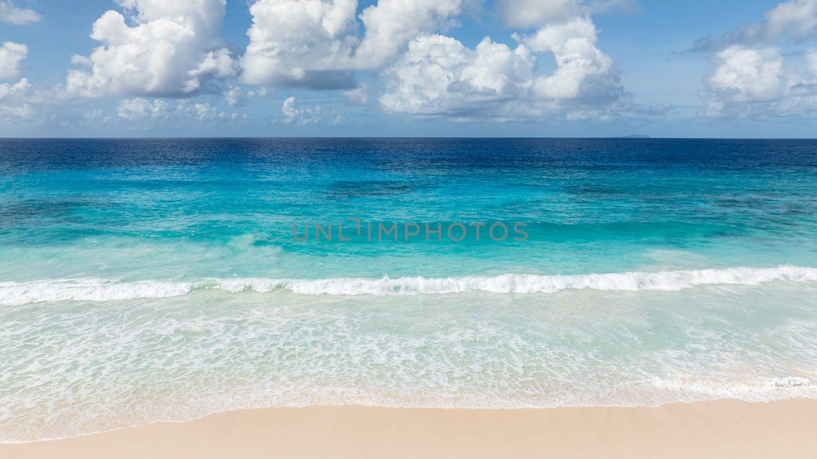 Turquoise waters and waves crashing onto a wide sandy beach. La Digue, Seychelles.