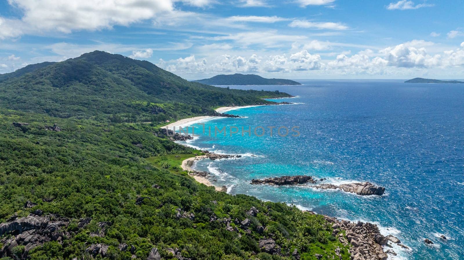 Waves roll onto the shore, hitting rocky formations with tropical greenery. La Digue, Seychelles.