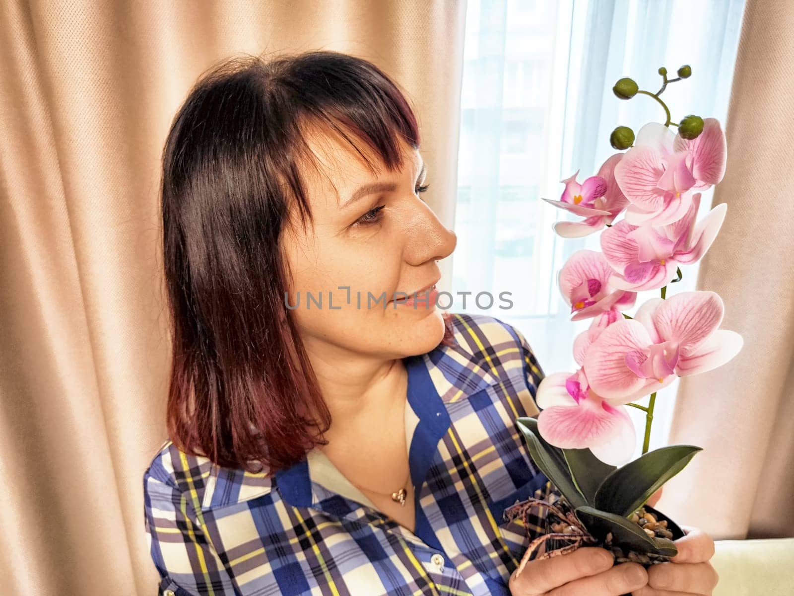A middle-aged psychologist smiles while holding a beautiful pink orchid in her office, with sunlight streaming through a window.