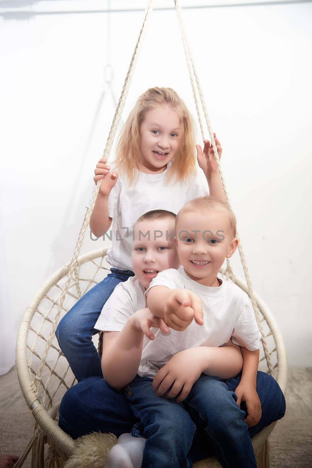 Three cheerful kids are enjoying their time on a cozy swing, sharing laughter and fun in a lively indoor space.