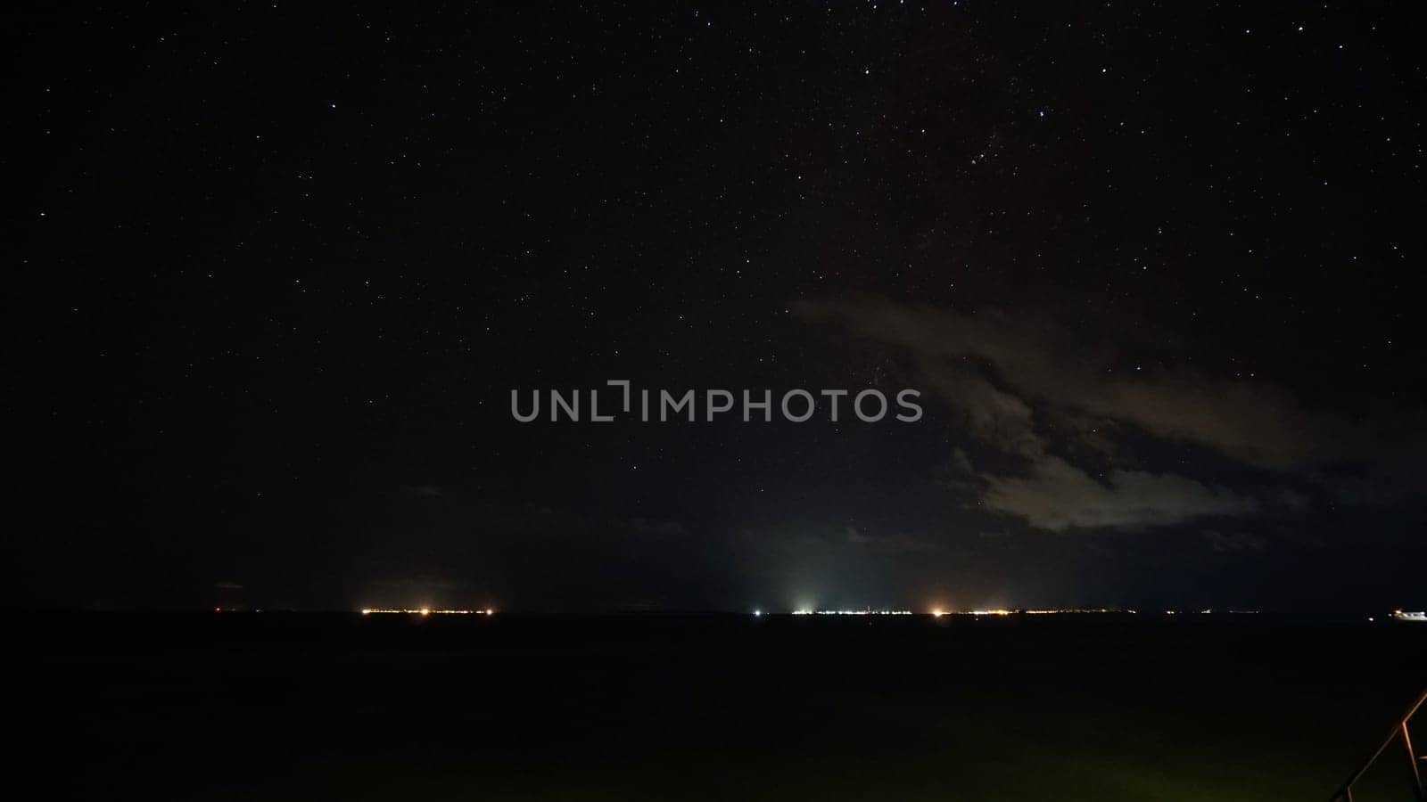 Breathtaking view of a starry night sky over a calm ocean, with the faint glow of distant city lights on the horizon creating a serene and magical atmosphere