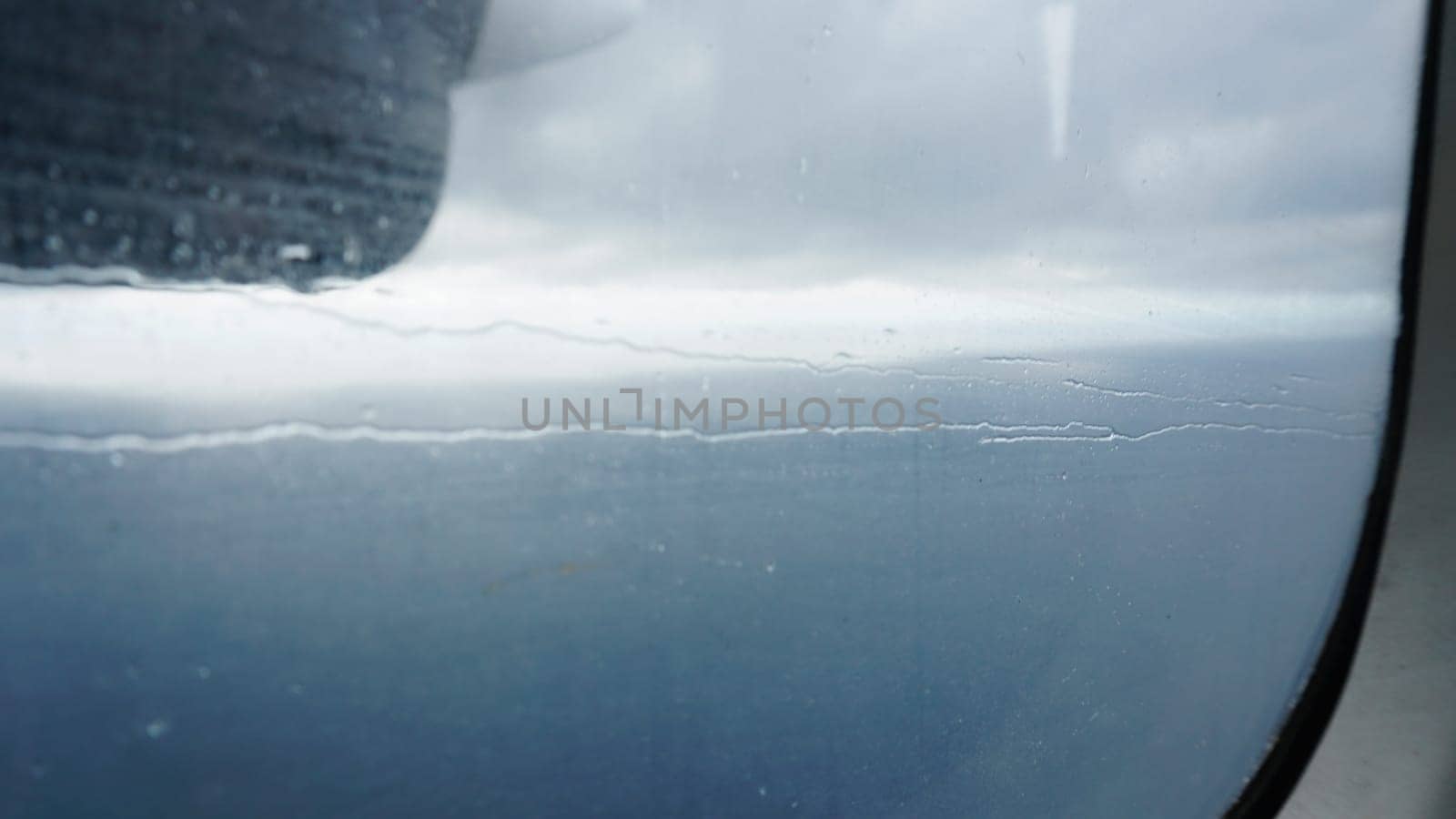 Rain falling on an airplane window during a flight over the ocean creates a captivating display of water droplets, forming intricate patterns against the backdrop of the sky