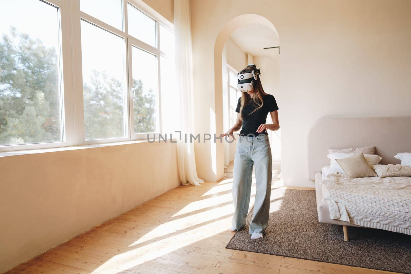 A person explores a virtual reality environment while wearing a headset in a spacious and sunlit room. The modern interior features light-colored walls and simple furniture.