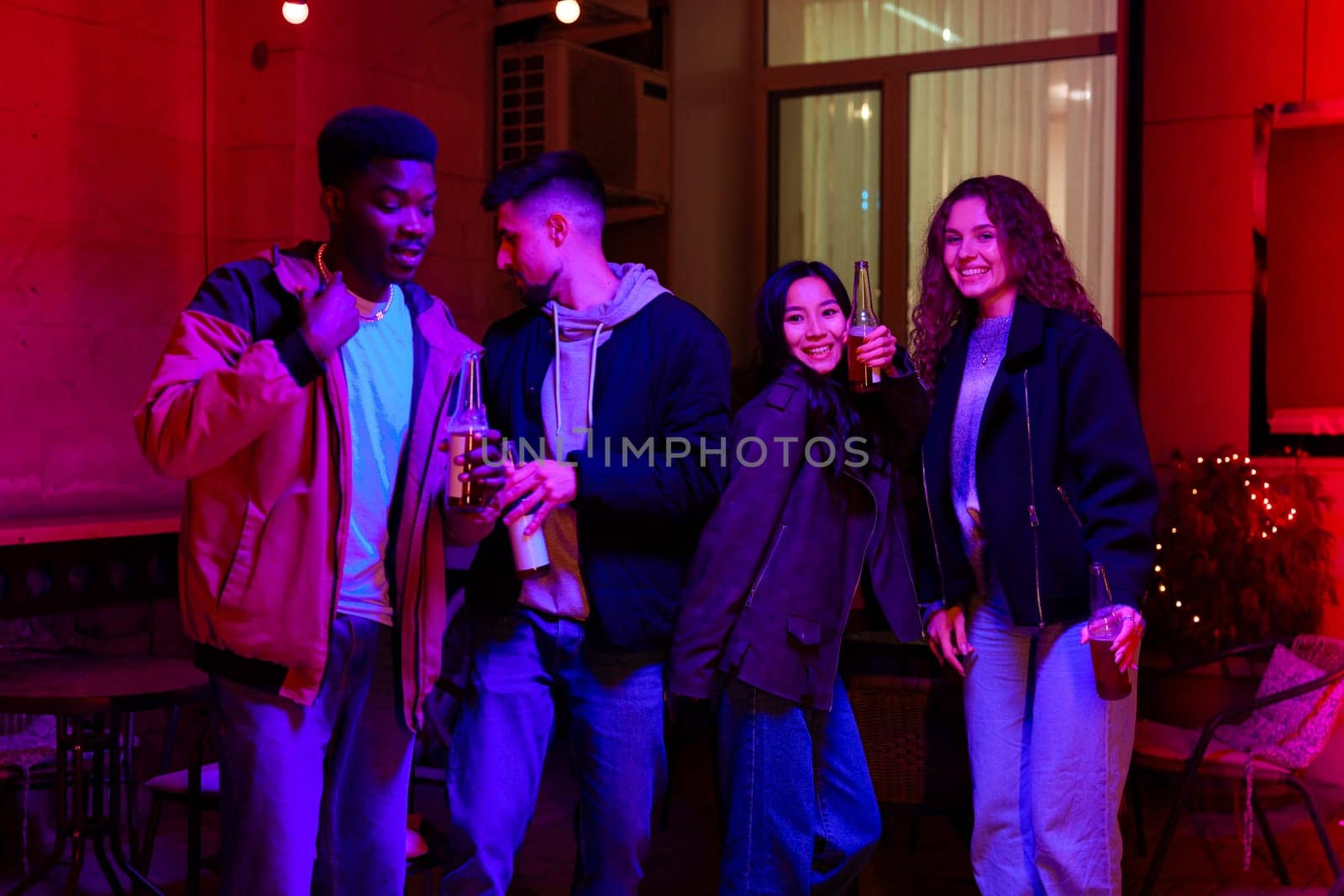 Four friends gather in a vibrant setting, laughing and sharing drinks. The warm glow of the lighting creates a cheerful atmosphere, perfect for socializing.