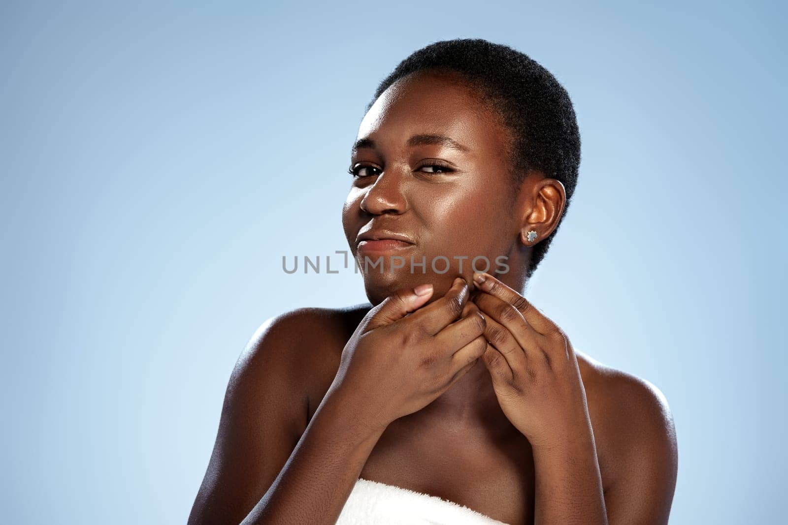A young woman with short hair smiles confidently while touching her chin. She is engaged in a skincare routine, highlighting her natural beauty in a bright setting.
