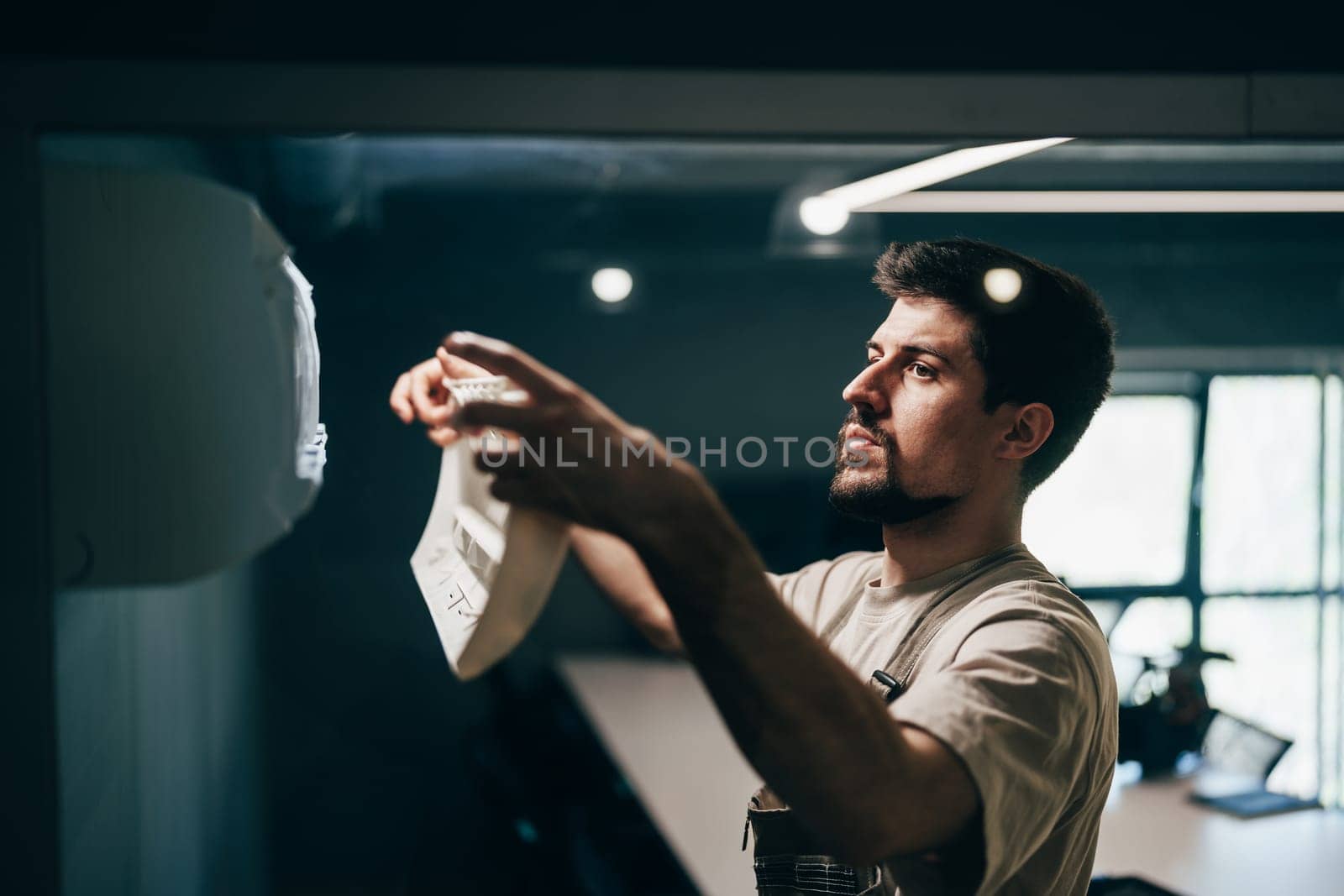 A man is carefully applying a decorative element to a wall in a well-lit modern workspace. Natural light fills the room, creating a vibrant atmosphere for creativity.