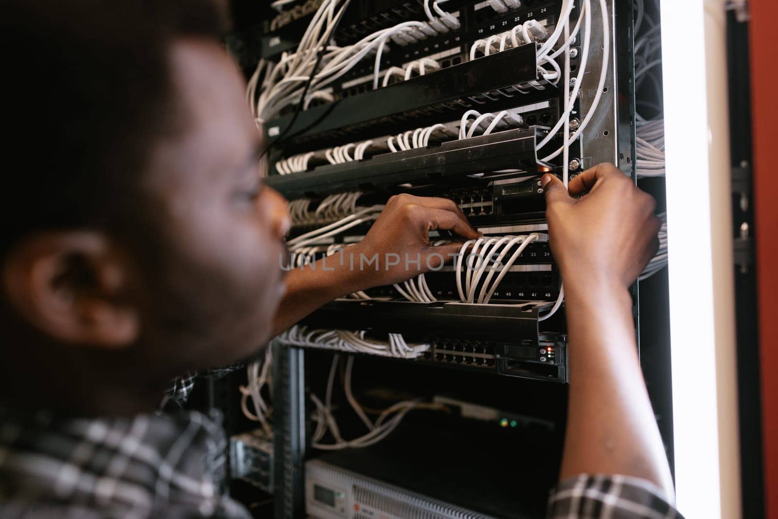 A technician is adjusting cables and securing connections on a server rack inside a data center. The environment is busy, with various network equipment visible.
