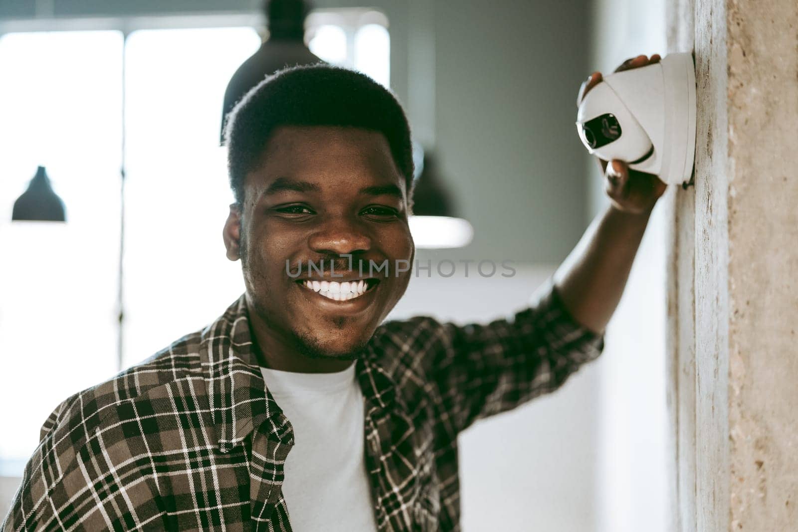 A man happily mounts a security camera on the wall of a bright office environment. Sunlight shines through the windows, enhancing the workspace's modern feel.