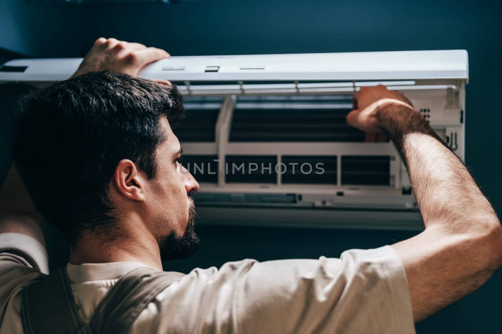A technician works on a wall-mounted air conditioning unit in a contemporary room. He carefully adjusts the inner components to ensure optimal performance and efficiency.